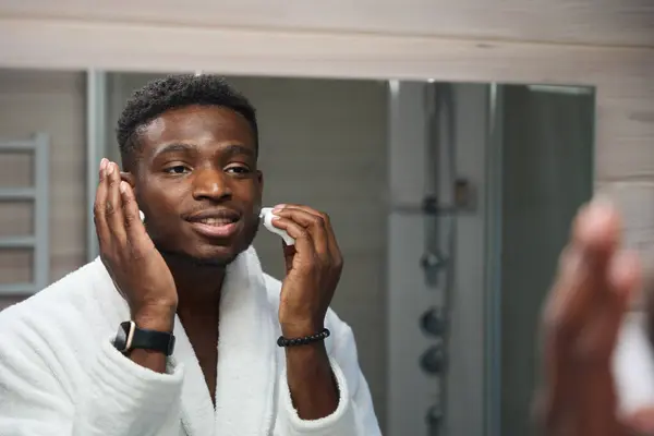 若い男は彼の顔に泡を剃ることを適用し 彼はバスルームで朝のルーチンをしています — ストック写真