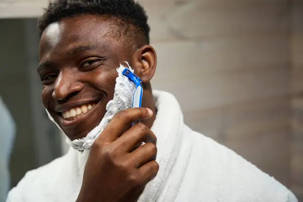 使い捨てカミソリが付いている笑顔のアフリカ系アメリカ人の男性の剃り 彼は剃る泡を使用します — ストック写真