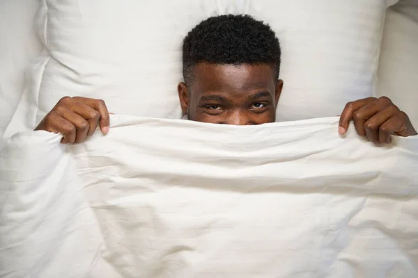 Happy African American Man Looks Out Blanket Lies Soft Bed — Stock Photo, Image