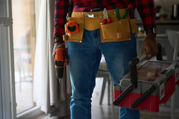 Male worker in a bright room with tools and a drill, a guy in a plaid shirt
