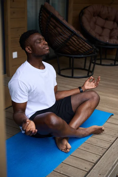African American male practices yoga on a wooden terrace, he meditates in the lotus position