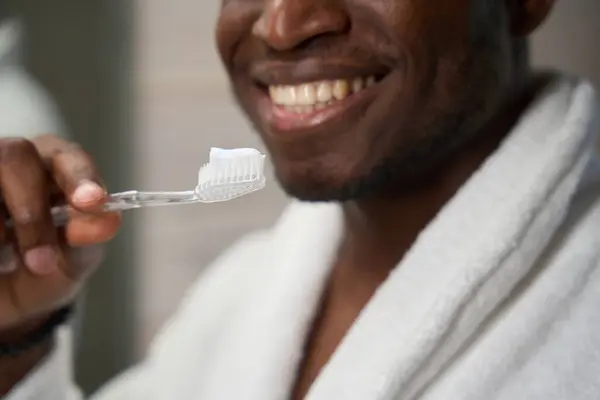 バスローブの男は歯磨きをする準備ができています 彼は歯ブラシと歯磨き粉を使用しています — ストック写真