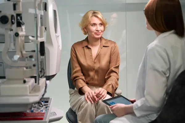 赤毛眼科医がレセプションで中年の女性に相談し 部屋には現代的なプロのデバイスがあります — ストック写真
