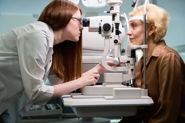 Uzman göz doktoru, çalışmalarında modern ekipman kullanır. Müşteri makinenin karşısında yer alır.
