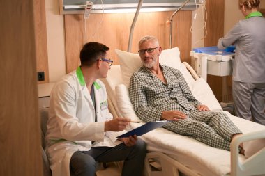 Terapist hastane koğuşunda yaşlı bir adamla iletişim kuruyor.