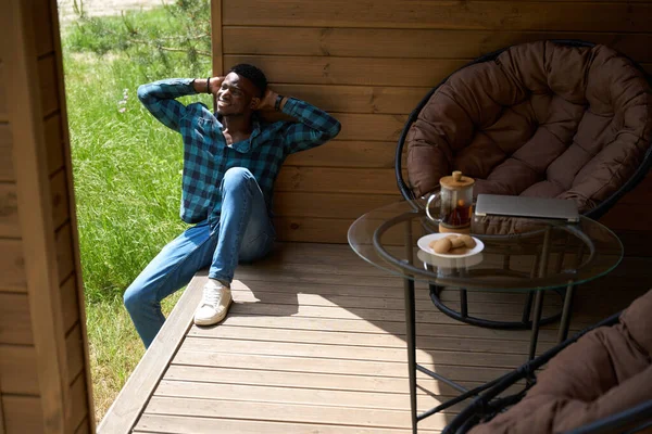 Man in comfortable clothes sits on a wooden terrace, morning tea is served on a table