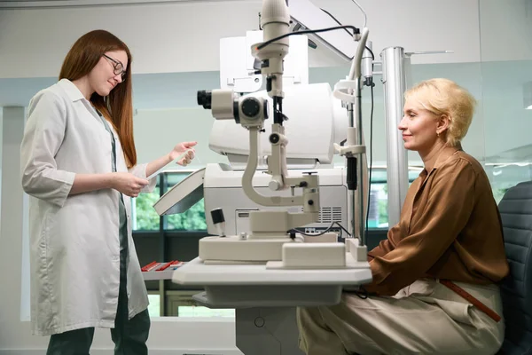 眼科医の任命で優雅な慎重な女性 医者は仕事で現代装置を使用しています — ストック写真