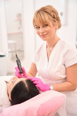 Alımlı sarışın müşteriye kaş dövmesi yapıyor, sanatçı koruyucu eldivenlerle çalışıyor.