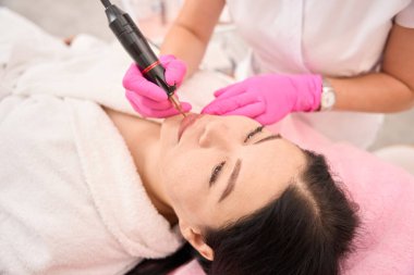 Uzman, özel bir aygıt kullanarak bir istemciye kalıcı dudak makyajı uygular