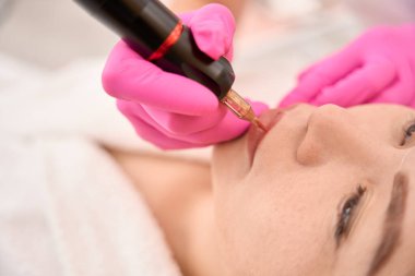 Koruyucu eldivenli güzellik uzmanı, özel bir cihaz kullanarak müşterisine kalıcı makyaj uygular.