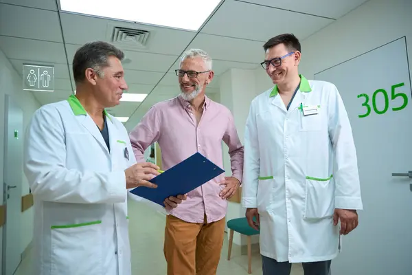 Usmívající Muži Komunikují Nemocniční Chodbě Diskutují Pojistných Papírech — Stock fotografie