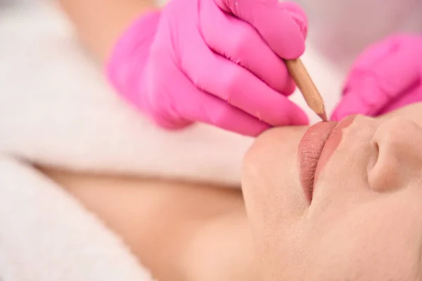 Marking a woman lips before a tattoo procedure, a specialist uses a pencil