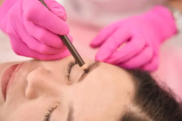 Master makes markings before the procedure of tattooing the eyebrows of a client, the master works in protective gloves