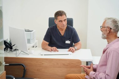 Experienced therapist communicates with an old man in a doctors office, the room has a minimalist interior clipart