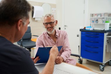 Doktor ofisinde evrakları imzalayan sakallı adam, büro masasında oturan adamlar.