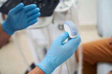 Doktor bir tıbbi tesiste ultrason makinesinde çalışıyor. Bir hasta yakınlarda oturuyor.