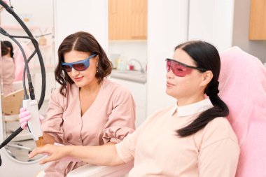 Bir kozmetoloji kliniğinin müşterisi parmaklar için lazer tüy çıkarma prosedürü uyguluyor, güvenlik gözlüğü takan insanlar...