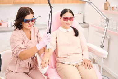 Kozmetik uzmanı ve koruyucu gözlüklü bir kuaför elleri için lazer tüy çıkarma prosedürü uyguluyor.