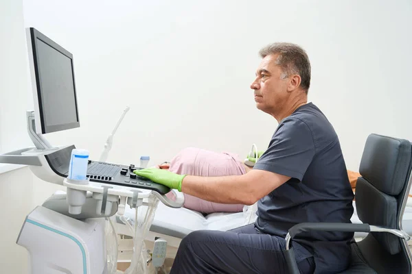 Ultrasound technician conducts an ultrasound examination on an elderly man, the diagnostician uses modern equipment
