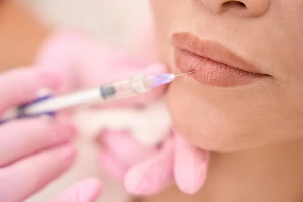 Injection lip rejuvenation procedure in a cosmetology salon, a specialist works in protective gloves