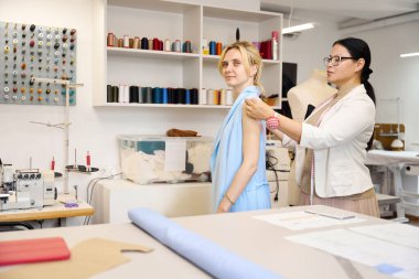 Müşteri dikiş atölyesinde usta olmaya çalışıyor. Odada bir sürü dikiş malzemesi var.