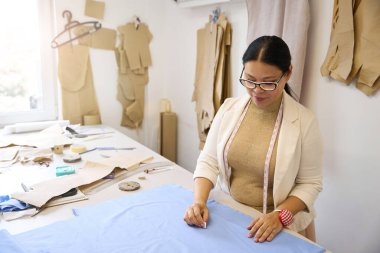 Kadın tasarımcı kesim masasında mavi kumaşla çalışıyor, kadın tebeşir kullanıyor.