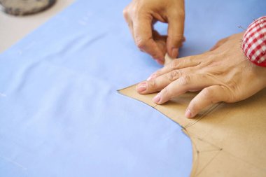 Dressmaker mavi kumaş üzerinde tebeşirle bir desen izler, işyeri iyi aydınlatılmış.