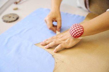 Sanatçı kadın mavi kumaş üzerinde tebeşirle bir desen izler, işyeri iyi aydınlatılmış.