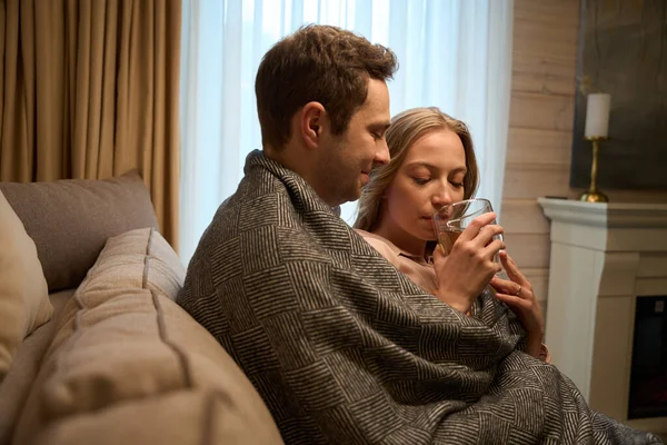 快乐的男人坐在沙发上 一边用毛毯抱着妻子 一边在家里喝茶 — 图库照片
