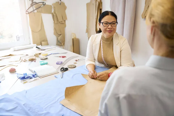 Tailoring master works with fabric and patterns and communicates with a woman fashion designer