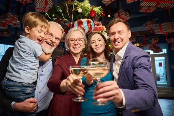 Happy festive family clinking glasses with champagne at Christmas dinner in cozy restaurant