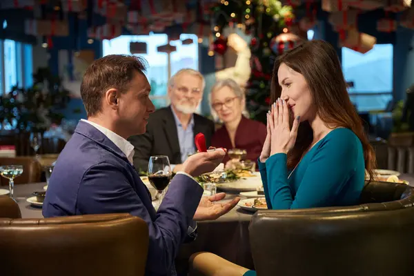 レストランのクリスマスディナーでテーブルに座っている間 赤いボックスを持つ男性を見ている印象的な女性 — ストック写真