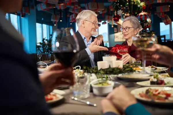 Happy man giving present to woman during festive dinner in restaurant on New Year Eve