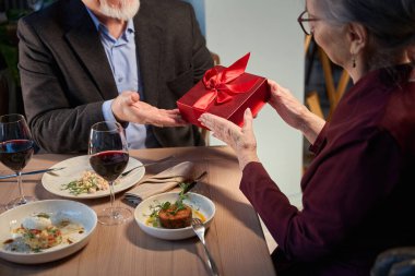 Tanınmayan yaşlı çift, yeni yılı kutluyor. Kadın, restoranda otururken hediye kutusunu erkeğe veriyor.