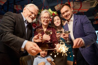 Noel ağacının yanında maytap ve şampanya kadehleriyle yeni yılı restoranda kutlayan neşeli bir aile.