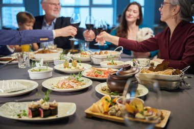 Restoran masasında nefis yemekler. İnsanlar bayramı kutlamak için arka planda şarap kadehleri kaldırıyor.