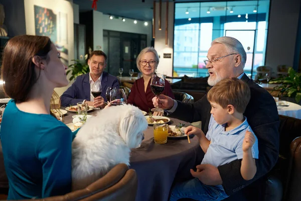 Aged man toasting with glass of wine during New Years Eve family celebration in restaurant