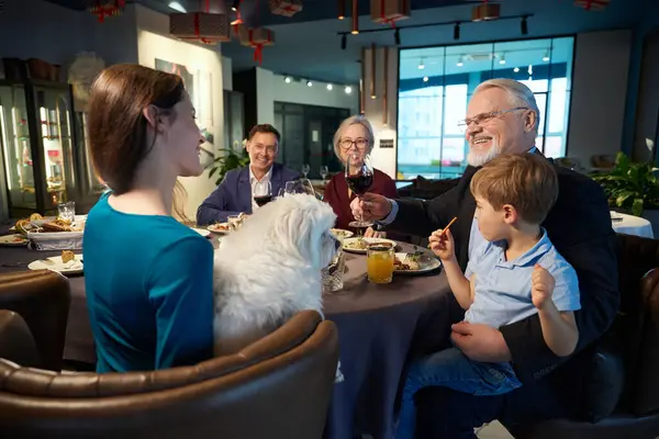 Smiling old man with glass of wine talking with family while celebrating Christmas in restaurant