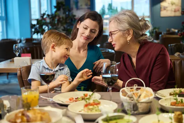 Cheerful aged woman talking with little boy enjoying Christmas dinner with her family in restaurant