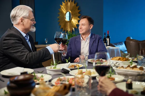 Joyful men with glasses of wine toasting in restaurant at New Year dinner enjoying festive holiday atmosphere