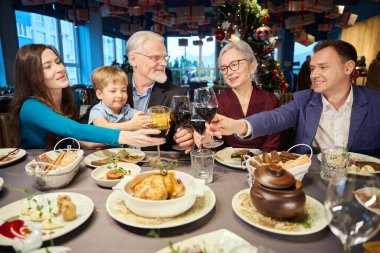 Gülümseyen aile bardaklarını tokuşturur. Restoranda Noel kutlaması yapıyorlar. Şenlikli yemekler yiyorlar.