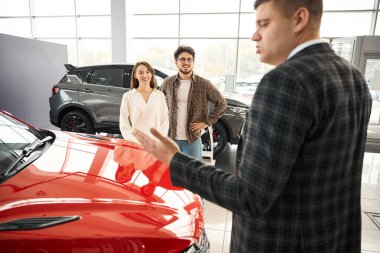 Satıcı kadın ve erkek için galeride otomobil sunuyor. Yeni bir araba almak istiyor.