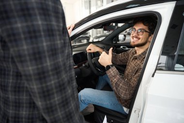 Otomobil galerisinden yeni araba alan mutlu bir adam oto galerisinde satış temsilcisine parmağını gösteriyor.