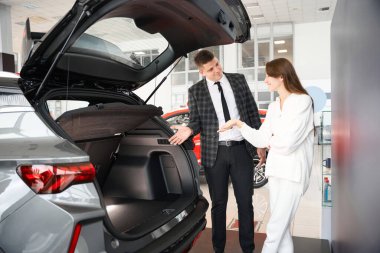 Araba galerisinde araba satan kendine güvenen bir satıcı kadın müşteriye özel teklifler sunuyor.