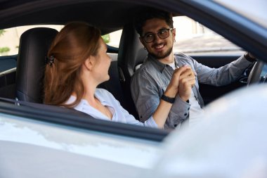 Genç, beyaz bir adam ve kadın el ele tutuşup otomobilde birbirlerine bakıyorlar. Romantik ilişki kavramı. Yolculuk, seyahat ve tatil fikri