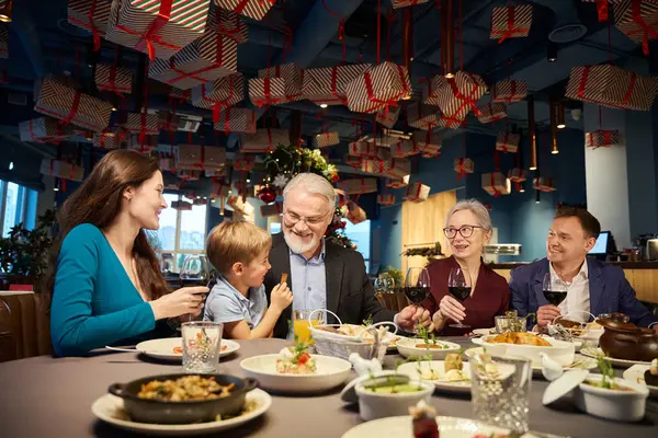 Overjoyed family sitting at table with glasses of wine celebrating Christmas congratulating each other