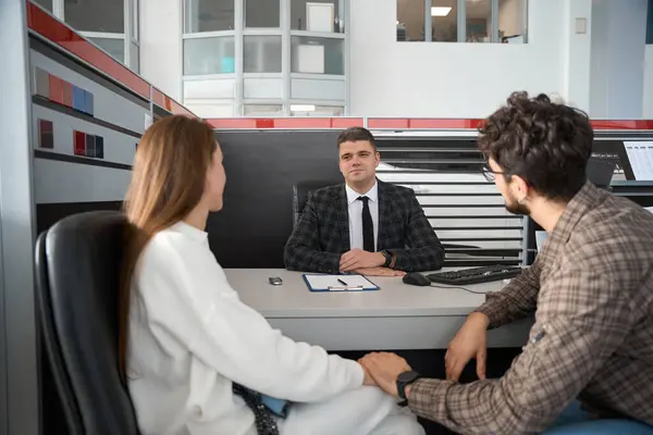 Happy woman and man signing some documents of car purchasing at table with salesperson in dealership office