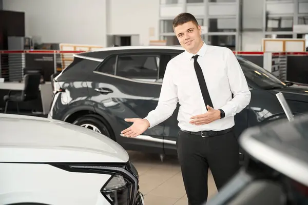 Sales manager standing in car showroom presenting new model of automobile in dealership
