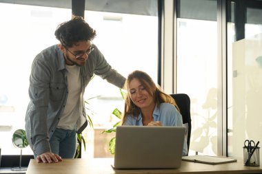 Young smiling caucasian businessman and businesswoman watching on laptop during work in sunny office. Concept of teamwork