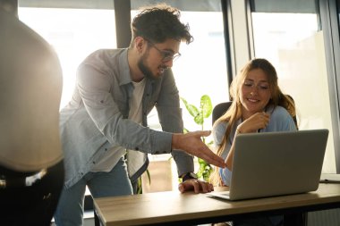 Young caucasian businessman showing something on laptop to his female colleague during work in sunny office. Concept of teamwork